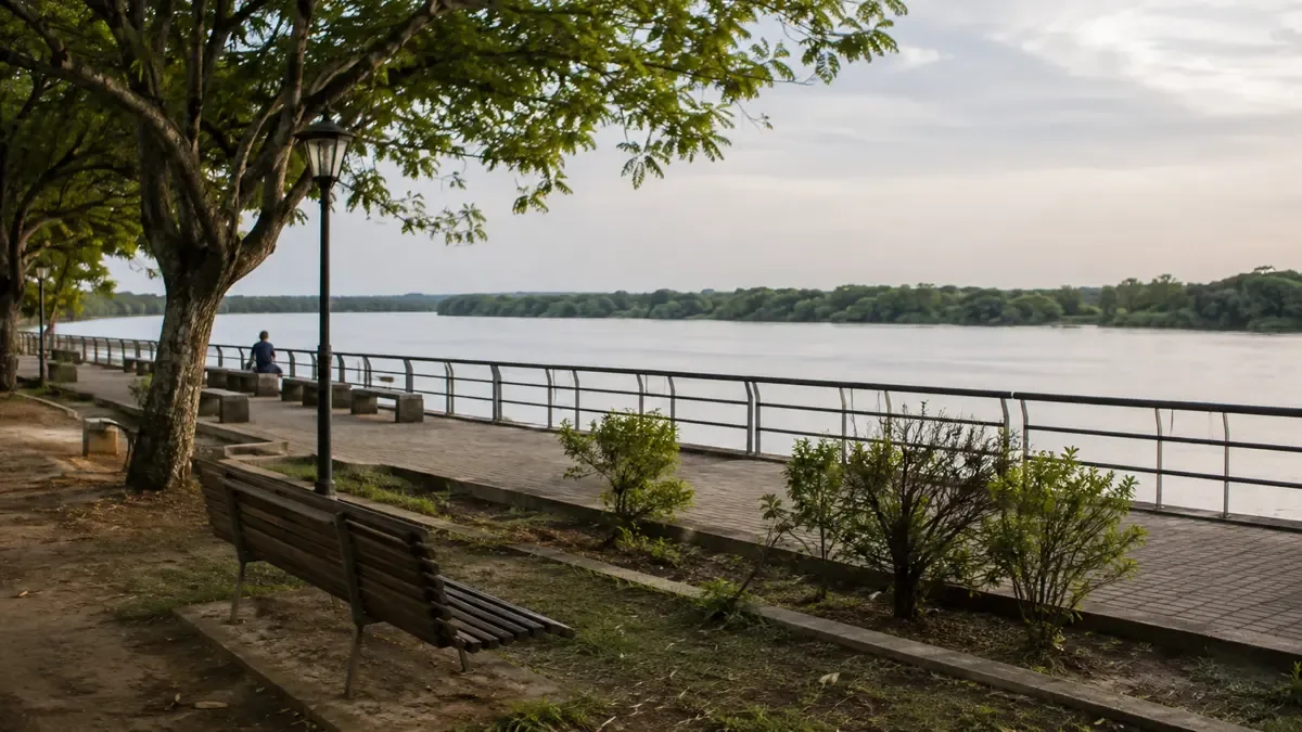 La ribera de un gran río con barandas y arbolado en una plaza de barrio con mobiliario urbano, vista en tres cuartos, profundidad de campo suave